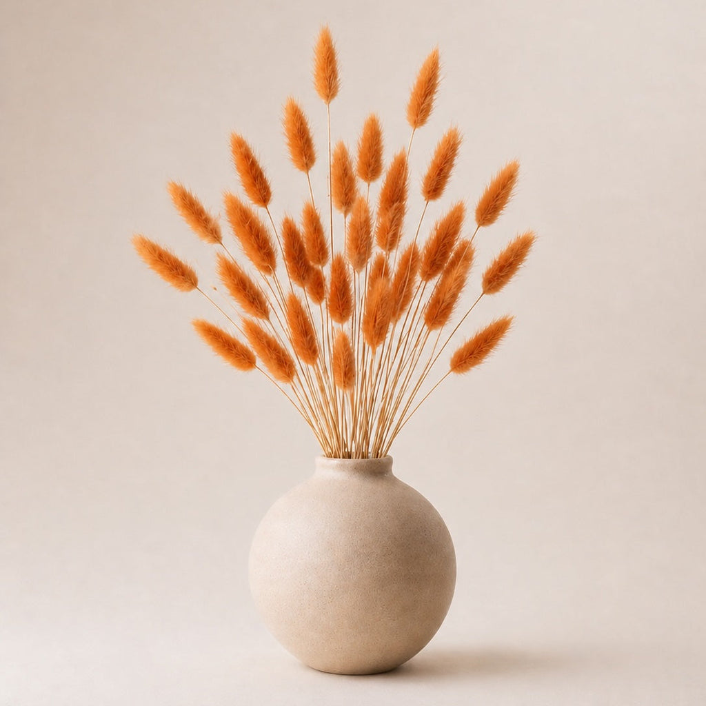 Ceramic vase with dried orange bunny tail plants on a beige background