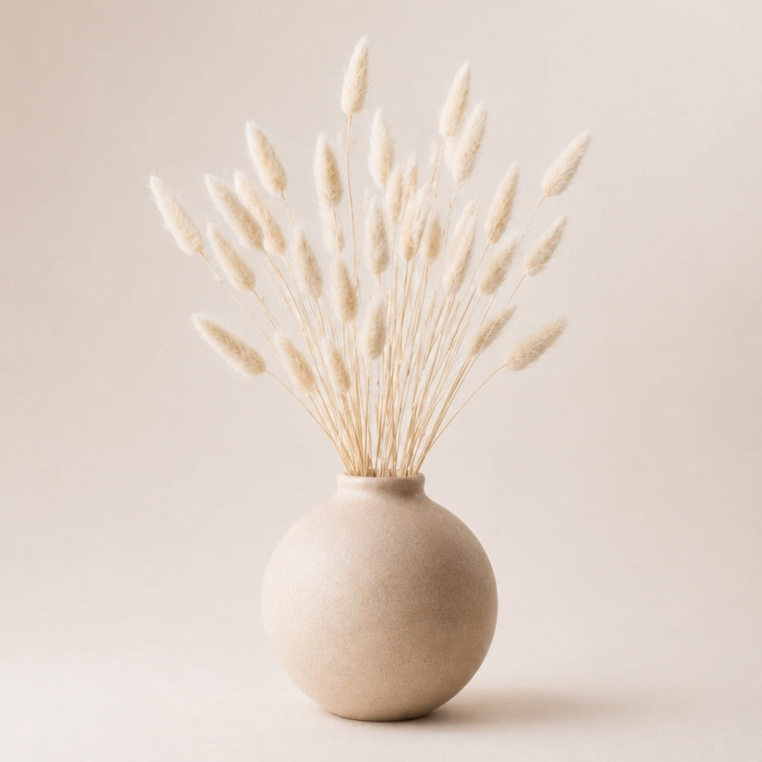Beige vase with dried grasses on a light beige background